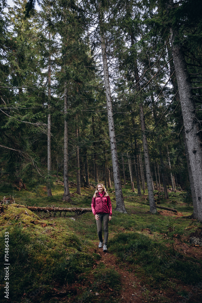 a woman in a pink jacket travels through the mountains. go on a hike with friends. a woman stands in the middle of a spruce forest