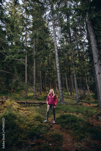a woman in a pink jacket travels through the mountains. go on a hike with friends. a woman stands in the middle of a spruce forest © Anhelina Tyshkovets
