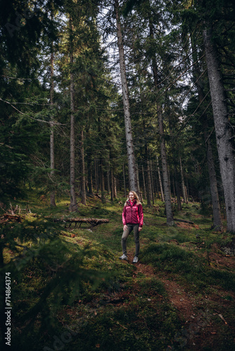 a woman in a pink jacket travels through the mountains. go on a hike with friends. a woman stands in the middle of a spruce forest
