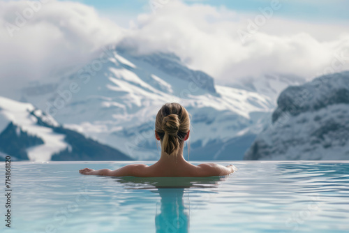 Woman relaxing in infinity pool and admiring winter mountains.