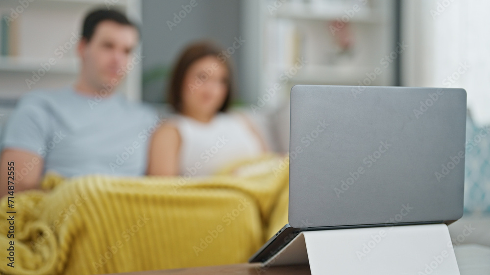 Beautiful couple watching movie on laptop sitting on sofa at home Beautiful couple watching movie on laptop sitting on sofa at home