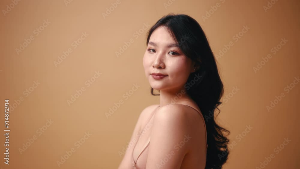 Portrait of a young Asian woman in beige lingerie posing on a beige background. The concept of skin care, cosmetology and spa treatments.