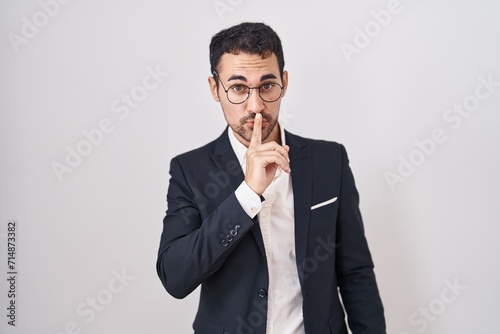 Handsome business hispanic man standing over white background asking to be quiet with finger on lips. silence and secret concept.