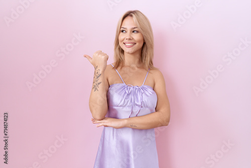 Young caucasian woman wearing lingerie dress smiling with happy face looking and pointing to the side with thumb up.