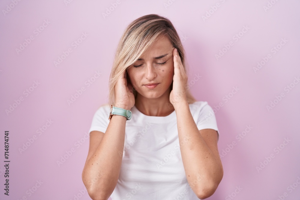 Young blonde woman standing over pink background with hand on head, headache because stress. suffering migraine. Young blonde woman standing over pink background with hand on head, headache because stress. suffering migraine.