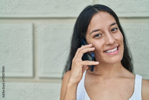 Young beautiful hispanic woman smiling confident talking on the smartphone over isolated white brick background