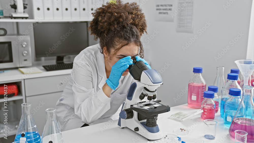 Hispanic woman with curly hair using a microscope in a laboratory setting, surrounded by scientific equipment. Hispanic woman with curly hair using a microscope in a laboratory setting, surrounded by scientific equipment.