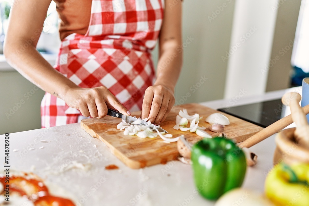 Young beautiful hispanic woman cutting onion at the kitchen