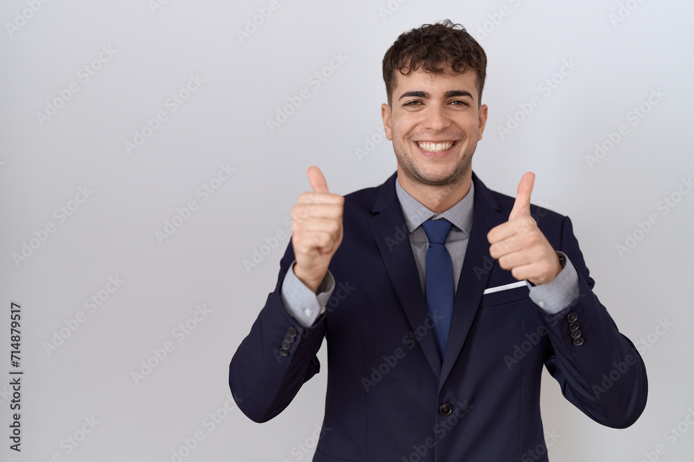 Young hispanic business man wearing suit and tie success sign doing positive gesture with hand, thumbs up smiling and happy. cheerful expression and winner gesture. Young hispanic business man wearing suit and tie success sign doing positive gesture with hand, thumbs up smiling and happy. cheerful expression and winner gesture.