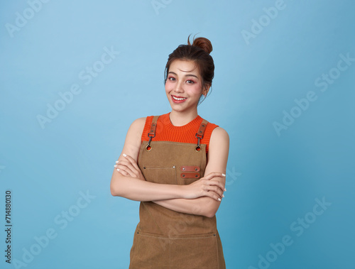 Portrait young asian barista woman wearing apron standing and smile arms crossed isolated on blue background, waitress or entrepreneur cheerful, small business or startup,