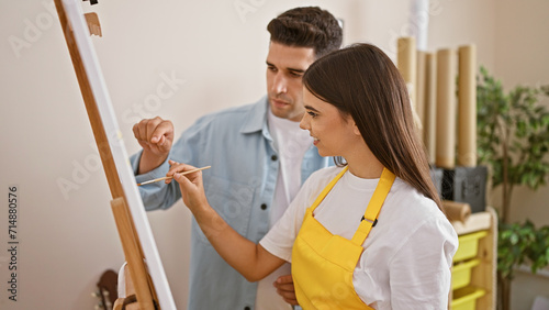 A woman and man, partners in a studio, collaborate while painting on the easel, immersed in creative teamwork.