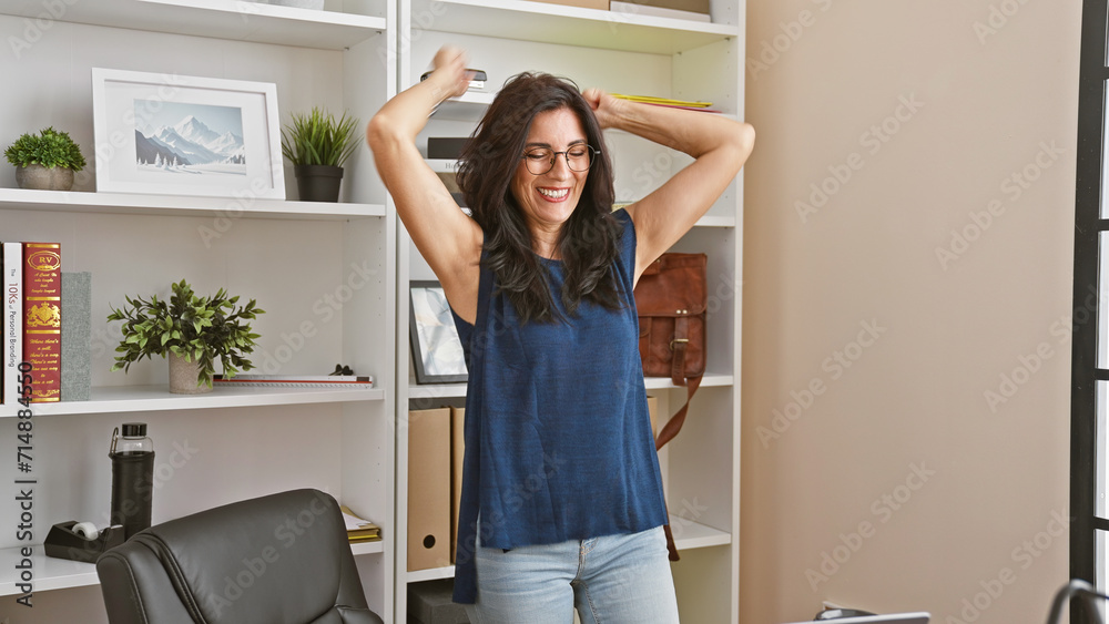 Happy mature hispanic woman stretching in a modern office, embodying work-life balance and job satisfaction