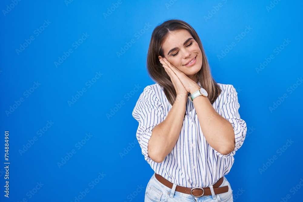 Hispanic young woman standing over blue background sleeping tired dreaming and posing with hands together while smiling with closed eyes. Hispanic young woman standing over blue background sleeping tired dreaming and posing with hands together while smiling with closed eyes.
