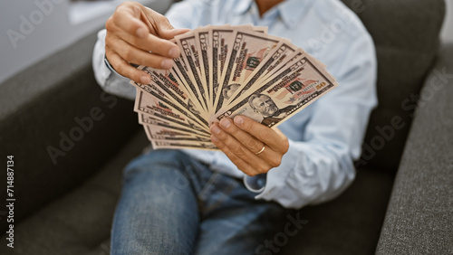 Obraz na plátně Handsome middle age man, a hard-working business professional, counting wealth in dollars at his office table, contemplating his successful investment strategy