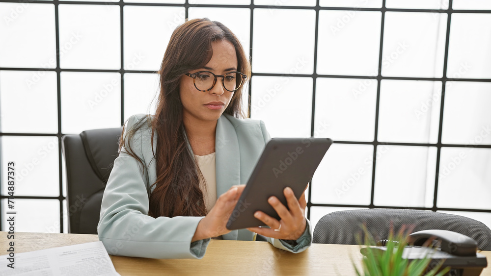 Hispanic beauty conquering the business world, young, hardworking female professional elegantly maneuvers her touchpad at the office Hispanic beauty conquering the business world, young, hardworking female professional elegantly maneuvers her touchpad at the office