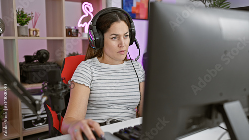 Focused young woman with headphones using a computer in a modern gaming room at night.