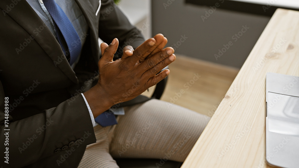 African american man in a suit gestures with his hands at an office setting, showing professionalism and confidence.