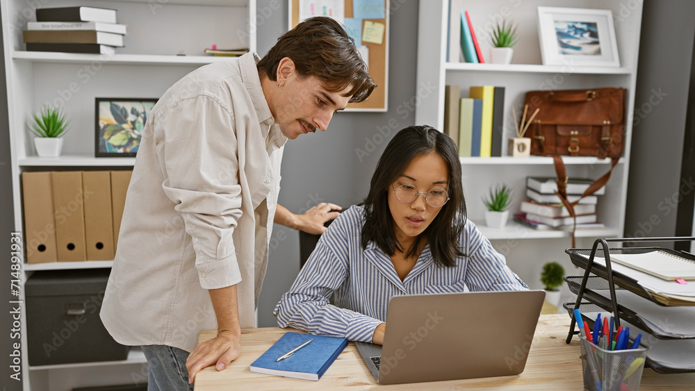 Coworkers, a man and a woman, collaborate in a modern office with a laptop and office supplies on the desk. Coworkers, a man and a woman, collaborate in a modern office with a laptop and office supplies on the desk.