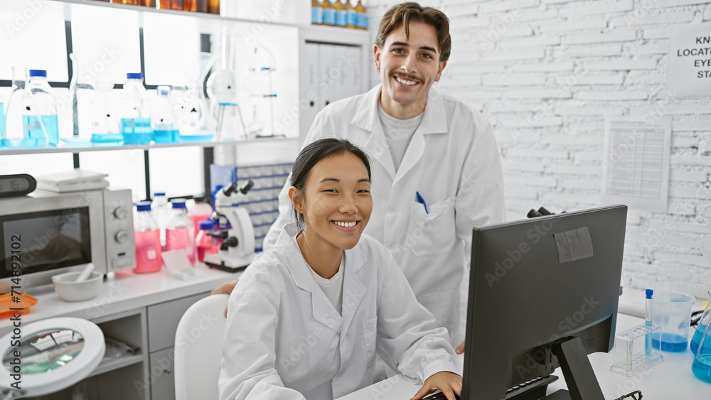 Man and woman in laboratory with computer, scientific equipment, and white coats