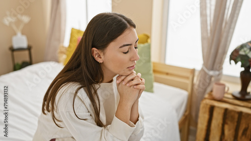 Young hispanic woman praying in a serene bedroom interior, portraying spirituality and tranquility at home.