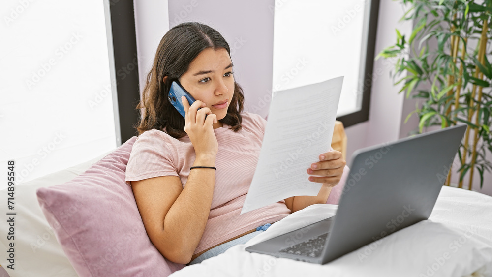 Hispanic young woman multitasking with phone and document in bedroom Hispanic young woman multitasking with phone and document in bedroom