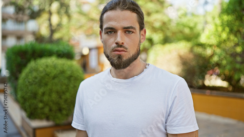 Young hispanic man standing  with serious expression at park