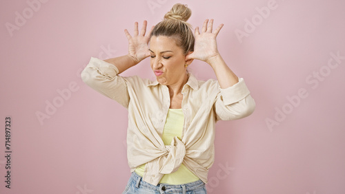 Young blonde woman doing derision expression with hands on ears over isolated pink background