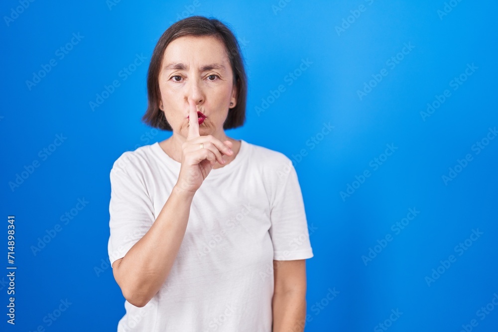Middle age hispanic woman standing over blue background asking to be quiet with finger on lips. silence and secret concept. Middle age hispanic woman standing over blue background asking to be quiet with finger on lips. silence and secret concept.