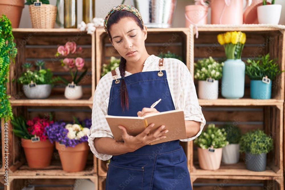 Young beautiful hispanic woman florist writing on notebook at florist