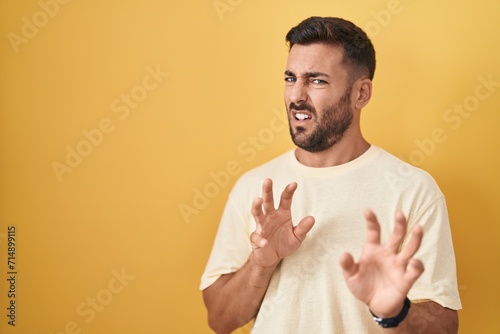 Handsome hispanic man standing over yellow background disgusted expression, displeased and fearful doing disgust face because aversion reaction. photo