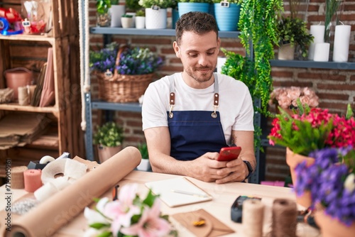 Young hispanic man florist smiling confident using smartphone at florist