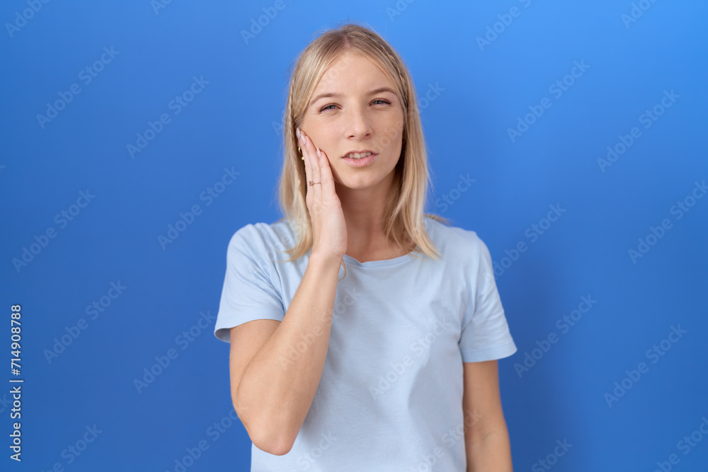 Young caucasian woman wearing casual blue t shirt touching mouth with hand with painful expression because of toothache or dental illness on teeth. dentist Young caucasian woman wearing casual blue t shirt touching mouth with hand with painful expression because of toothache or dental illness on teeth. dentist