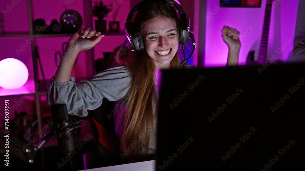 A jubilant young woman with headphones celebrates in a vibrant gaming room at night. A jubilant young woman with headphones celebrates in a vibrant gaming room at night.