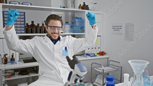 Young hispanic man scientist smiling confident using microscope celebrating at laboratory