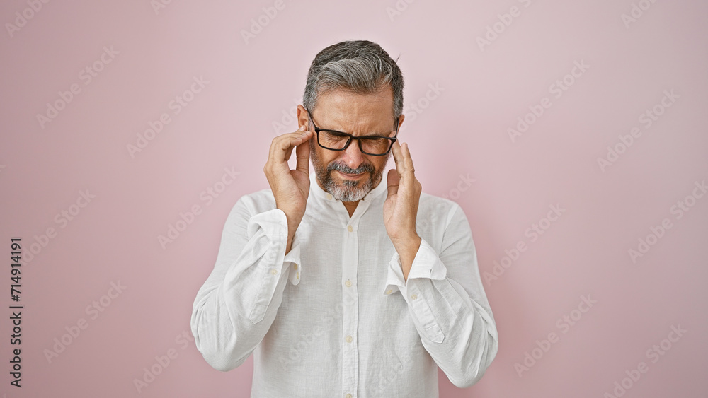 Stressed young hispanic man with grey-haired, suffering a heavy headache, alone over a pink isolated background, reflecting illness, sadness, and frustration Stressed young hispanic man with grey-haired, suffering a heavy headache, alone over a pink isolated background, reflecting illness, sadness, and frustration
