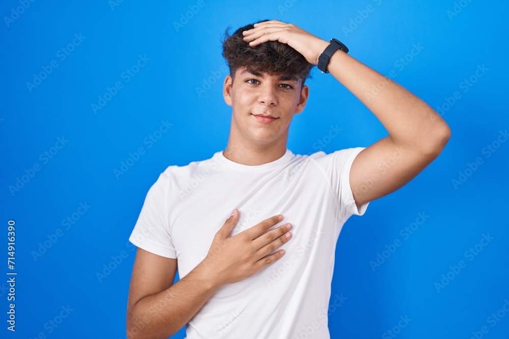 Naklejka premium Hispanic teenager standing over blue background touching forehead for illness and fever, flu and cold, virus sick