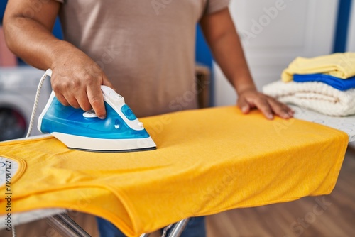 Young latin man ironing clothes at laundry room