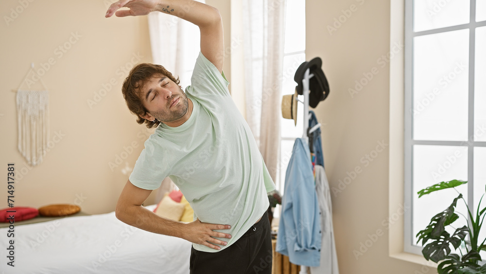 Handsome man stretching in a bright bedroom with plants and clothes rack. Handsome man stretching in a bright bedroom with plants and clothes rack.