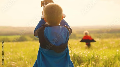 Boy plays with puppy, holds dog in his hands. Favorite Dog in arms of boy in park. Child loves and hugs dog. Owner of puppy and child play together in fresh air. Dog is childs friend. Walking with pet photo