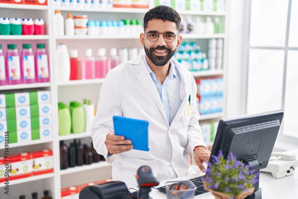 Young arab man pharmacist using touchpad and computer at pharmacy