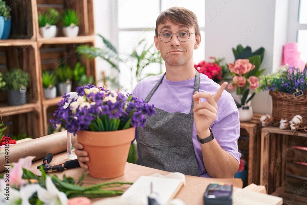 Caucasian blond man working at florist shop pointing aside worried and nervous with forefinger, concerned and surprised expression