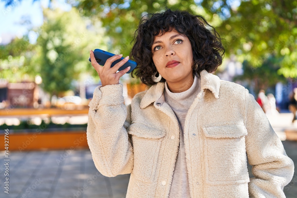 Fototapeta premium Young beautiful hispanic woman listening audio message by the smartphone with serious expression at park