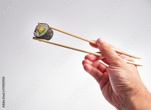 A man's hand skillfully holds a sushi roll with chopsticks against a white background, illustrating culinary dexterity and japanese cuisine.