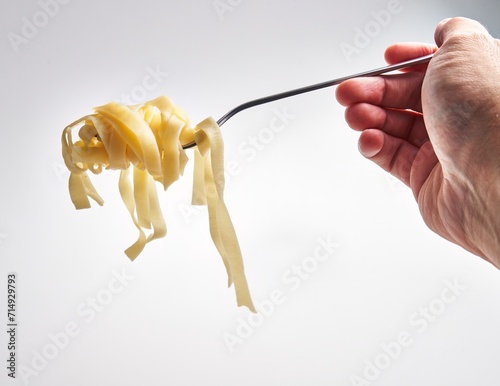 Close-up of a hand twirling fettuccine pasta on a fork against a white background, depicting italian cuisine.