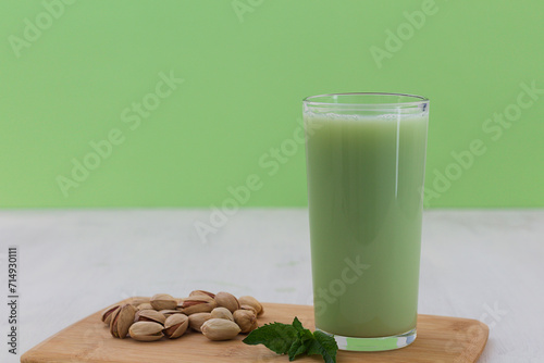 Alternative milk. glass of Natural plant based Pistachio milk with pistachionuts and green mint on the white table with green background. A paper straw in a glass. Healthy diet. copy space photo