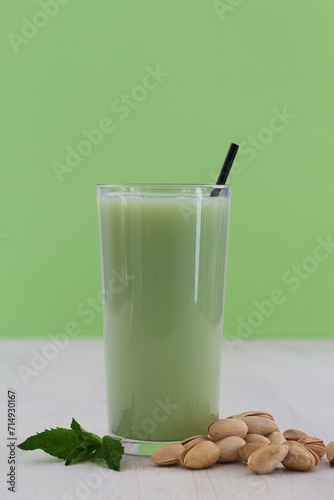 glass of Natural plant based Pistachio milk with pistachionuts and green mint on the white table with green background. A paper straw in a glass. Healthy diet. Alternative milk. copy space. vertical photo