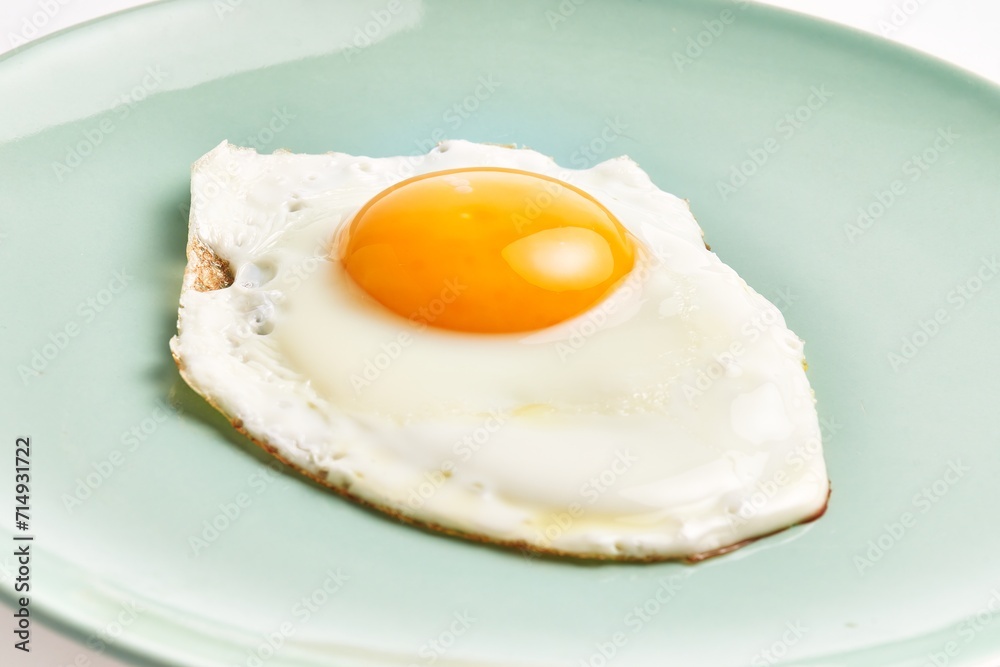 Close-up of a freshly cooked sunny side up egg on a pale blue plate against a white background. Close-up of a freshly cooked sunny side up egg on a pale blue plate against a white background.