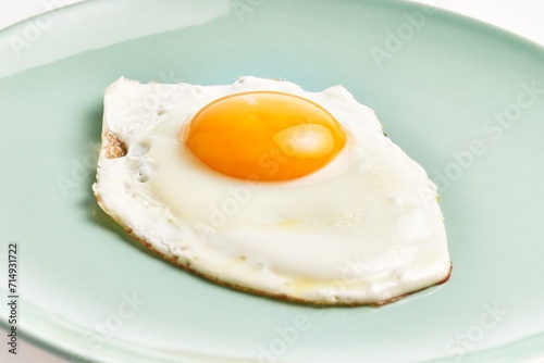 Close-up of a freshly cooked sunny side up egg on a pale blue plate against a white background.