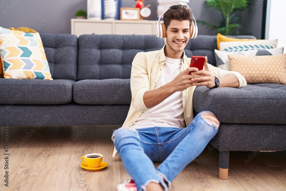 Obraz premium Young hispanic man listening to music sitting on floor at home