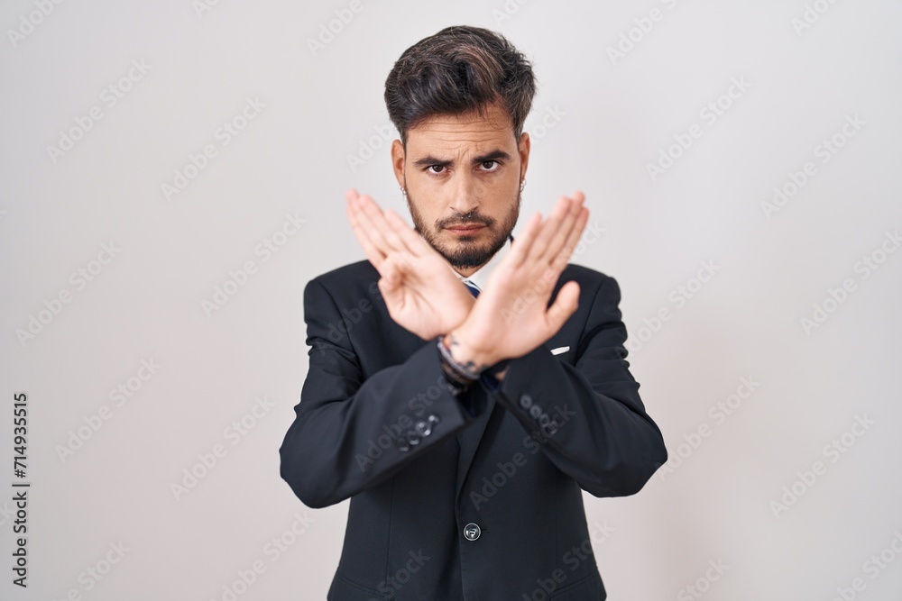 Young hispanic man with tattoos wearing business suit and tie rejection expression crossing arms and palms doing negative sign, angry face Young hispanic man with tattoos wearing business suit and tie rejection expression crossing arms and palms doing negative sign, angry face